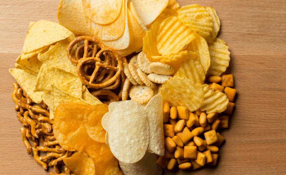 Variedade de alimentos ultraprocessados, como hambúrgueres, batata frita, refrigerante, donuts, chocolates, biscoitos e salgadinhos, mostrando produtos ricos em açúcar, gordura e aditivos.