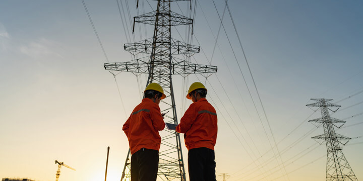 Engenheiros em frente a torres de transmissão de energia elétrica ao entardecer