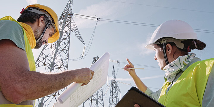 Engenheiros analisando projetos em frente a torres de transmissão da matriz energética elétrica