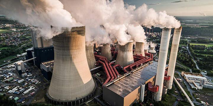 Imagem aérea de uma usina de carvão mineral, com torres emitindo vapor e fumaça ao redor