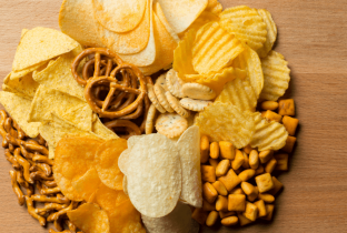 Variedade de alimentos ultraprocessados, como hambúrgueres, batata frita, refrigerante, donuts, chocolates, biscoitos e salgadinhos, mostrando produtos ricos em açúcar, gordura e aditivos.