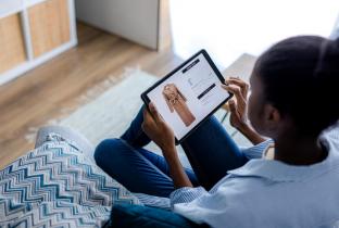 A imagem mostra uma jovem sentada no sofá, com expressão de frustração e confusão ao olhar para dentro de uma caixa de papelão aberta. Ela faz um gesto de insatisfação com a mão ao conferir o pedido. O cenário residencial reforça a experiência negativa do usuário no pós-venda, sendo ideal para ilustrar problemas com tamanho, qualidade ou avarias em compras de e-commerce internacional.