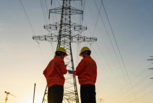 Engenheiros em frente a torres de transmissão de energia elétrica ao entardecer