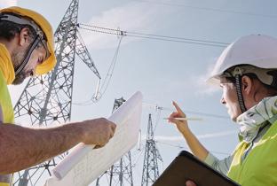 Engenheiros analisando projetos em frente a torres de transmissão da matriz energética elétrica