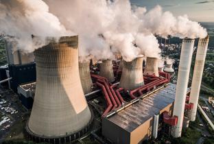 Imagem aérea de uma usina de carvão mineral, com torres emitindo vapor e fumaça ao redor